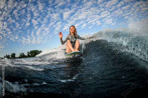 woman sits on wakesurf board and rides the wave and touches the waves with one hand