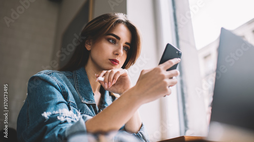 Thoughtful woman using smartphone in cafe