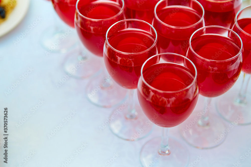 A row of glasses with red drinks, juice, champagne or wine at a party. Catering. Glassware on the table with a white tablecloth. Festive buffet for the holiday. A row of glasses with red drinks, juice, champagne or wine at a party. Catering. Glassware on the table with a white tablecloth. Festive buffet for the holiday.