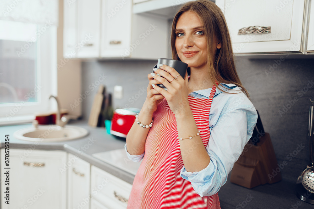 Pretty young woman in red apron enjoying a cup of coffee in her kitchen Pretty young woman in red apron enjoying a cup of coffee in her kitchen