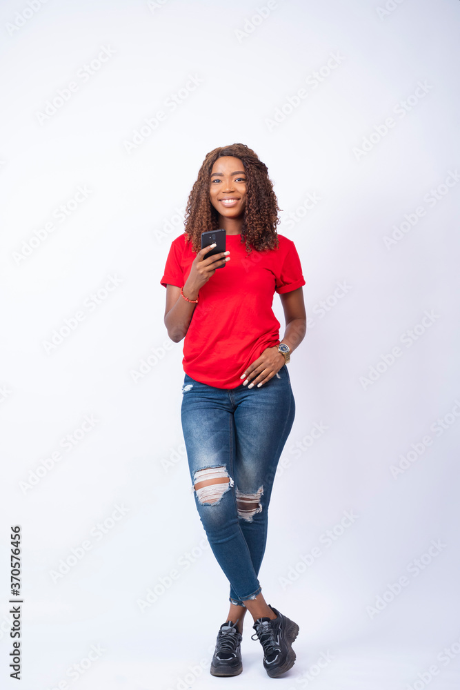 young pretty black lady standing with legs crossed holding her phone and smiling young pretty black lady standing with legs crossed holding her phone and smiling