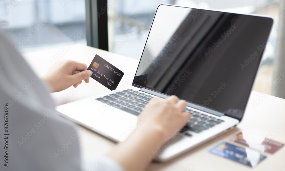 Young Asian man holds a credit card to make payments via laptop in his office.