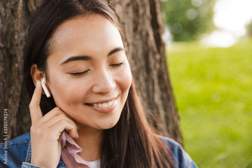 Image of joyful asian student woman using wireless earphones and smiling