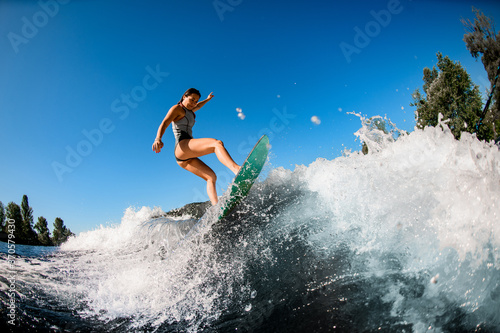 young wet woman energetically balancing on wave on wakesurf board