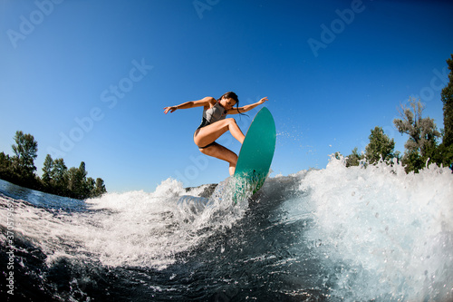 Photography young wet woman energetically balancing on wave on wakesurf board