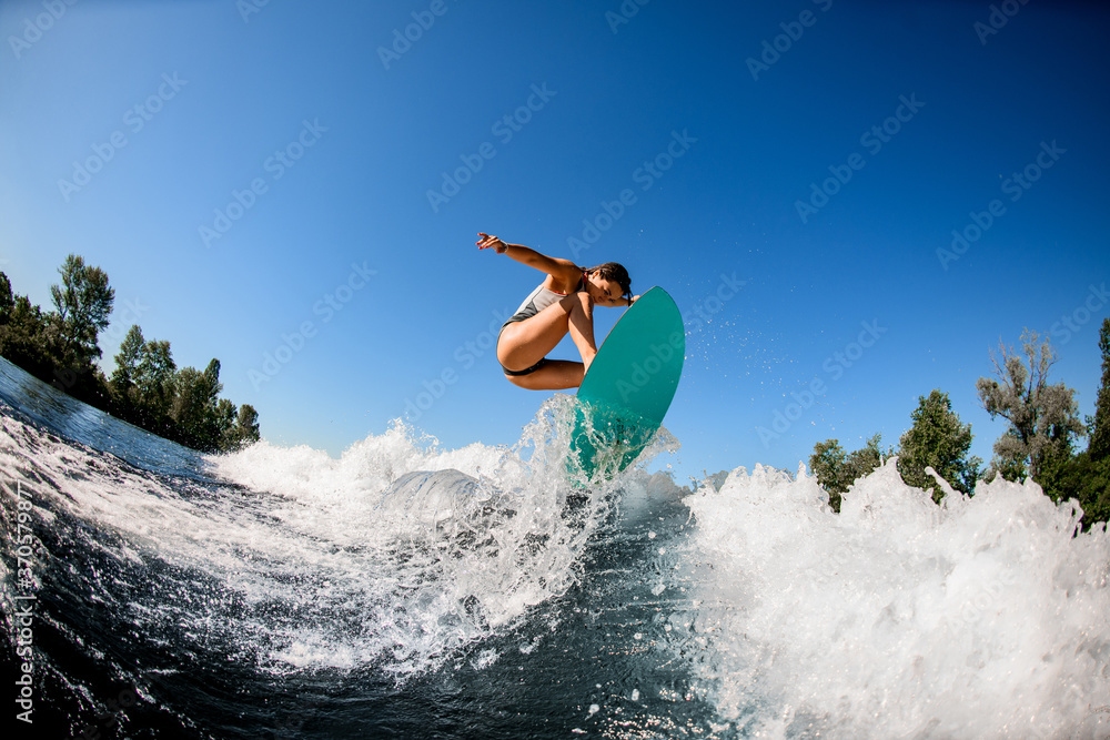 Woman wakesurfer in gray swimsuit jumps with bright surf board