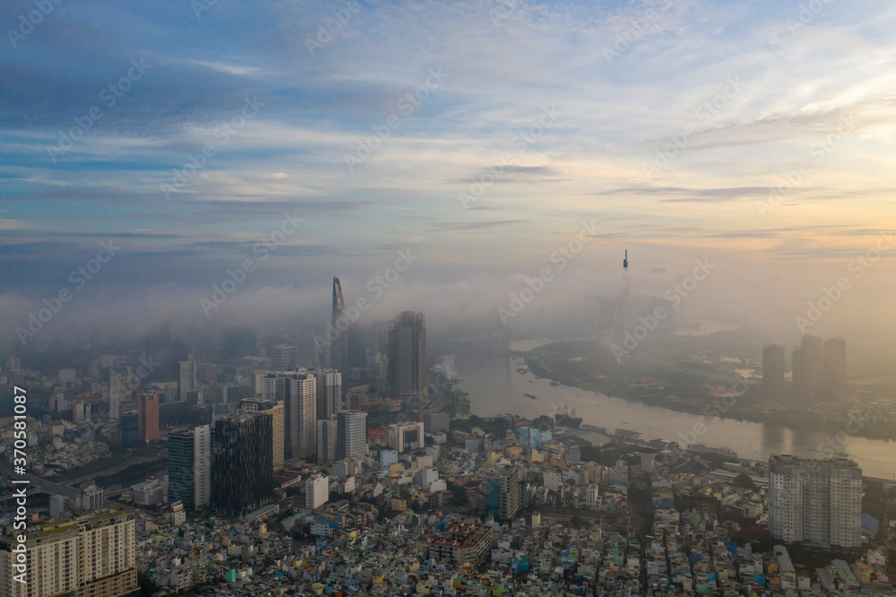 Dramatic aerial view of colorful sunrise and morning fog in Ho Chi Minh City featuring the Saigon River and landmark high rise buildings obscured by low cloud