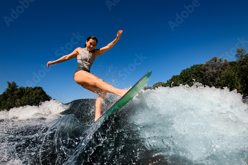 Side view of sporty woman who rides the wave on surfboard