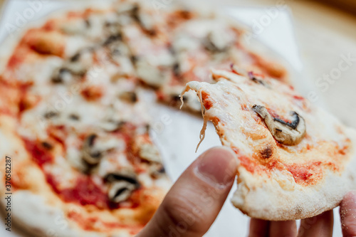 Hand holding a slice of a vegetarian pizza, with tomato sauce, mushrooms and mozzarella cheese