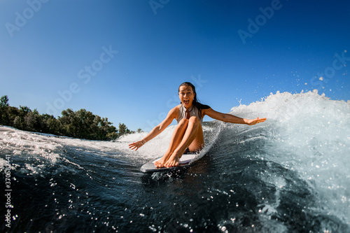 Surprisedly cheerful woman sits on wakesurf board and rides the wave