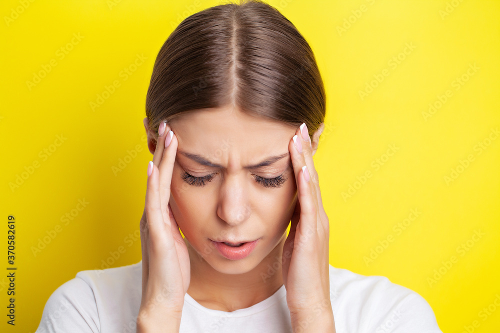 A young woman holds her hand near her head and feels a severe headache A young woman holds her hand near her head and feels a severe headache