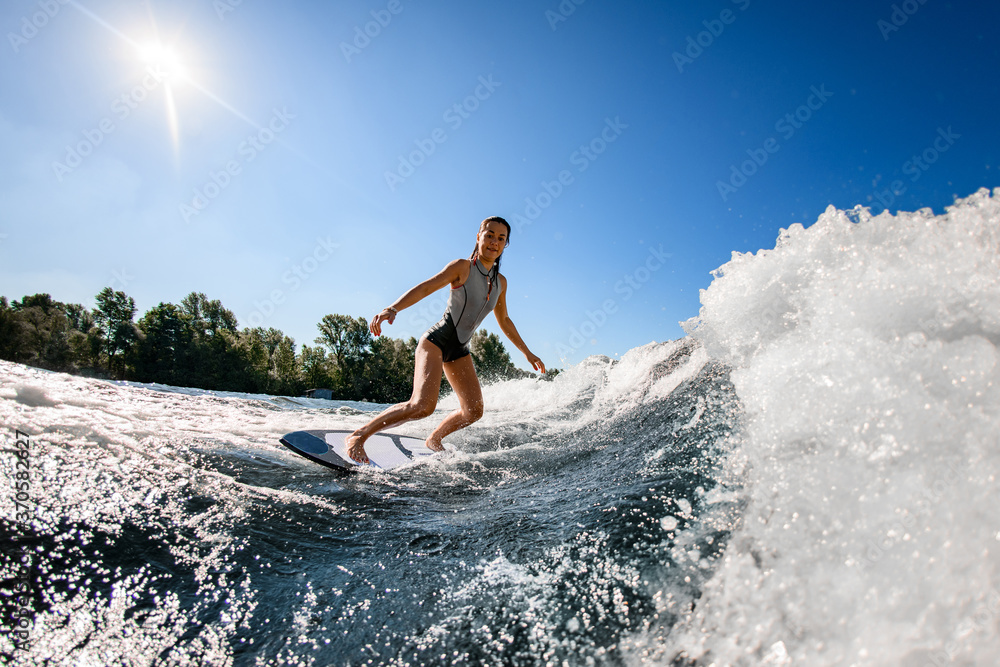 female wakesurfer in red swimsuit rides up the wave on surfboard