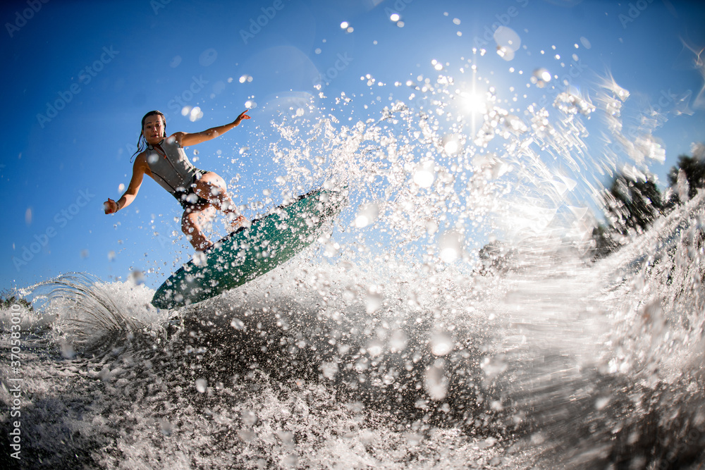 Naklejka premium gorgeous view of athlete woman in gray swimsuit who jumps with bright surf board.