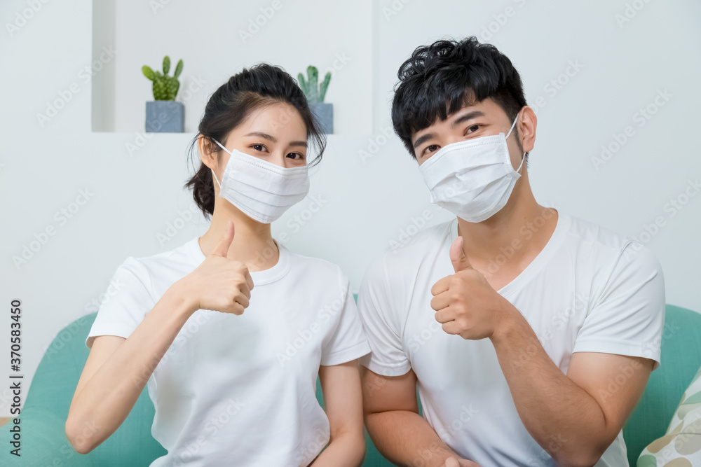 Asian couple wearing protective face mask and showing thumb up at home.
