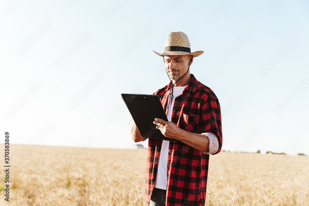Image of pleased adult man looking aside while standing at cereal field Image of pleased adult man looking aside while standing at cereal field