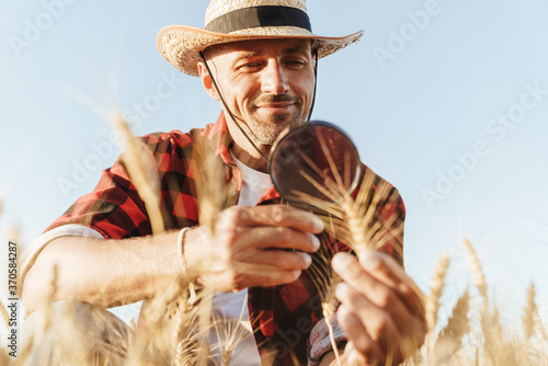 Image of pleased unshaven adult man examining harvest with magnifier