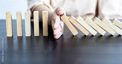Businessman's hand prevents Dominino from falling completely, solutions to prevent problems, find risk points that will cause business to fail.