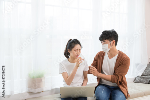 Couple wearing a protective face mask and woman working at home. But she got cold and flu, the man bringing her a hot drink and taking care of her.