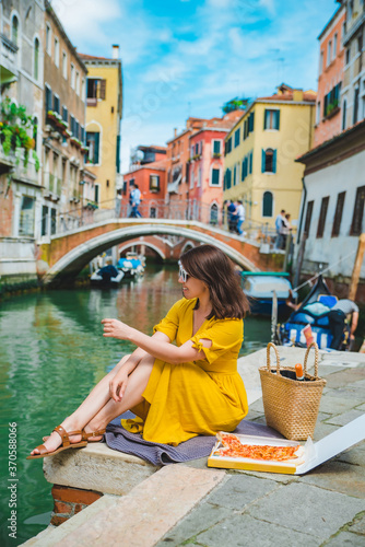 woman sitting on pond with view of venice canal eating pizza © phpetrunina14