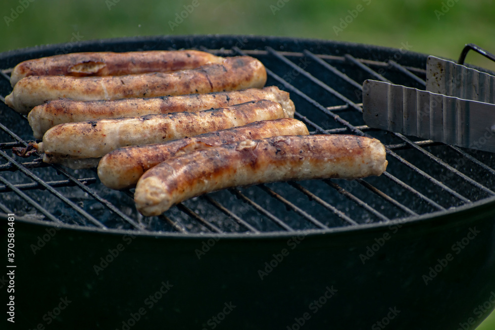 Delicious sausages frying on a grill outdoors.