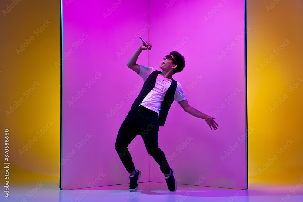 Star. Young male musician, singer performing on pink-orange background in neon light. Concept of music, hobby, festival, entertainment, emotions. Joyful party host, singer, portrait of artist.