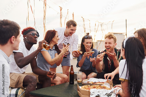 With delicious pizza. Group of young people in casual clothes have a party at rooftop together at daytime © standret