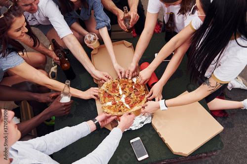 With delicious pizza. Group of young people in casual clothes have a party at rooftop together at daytime