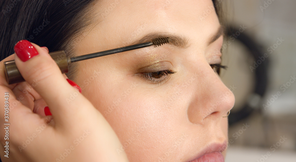 Eyebrow makeup close-up. Eye of a young woman during makeup, makeup artist paints with a brush the eyebrow.