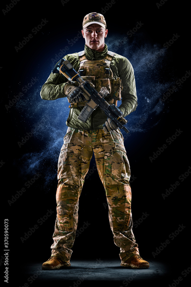 Army soldier in Protective Combat Uniform holding Special Operations Forces Combat Assault Rifle on dark background Army soldier in Protective Combat Uniform holding Special Operations Forces Combat Assault Rifle on dark background