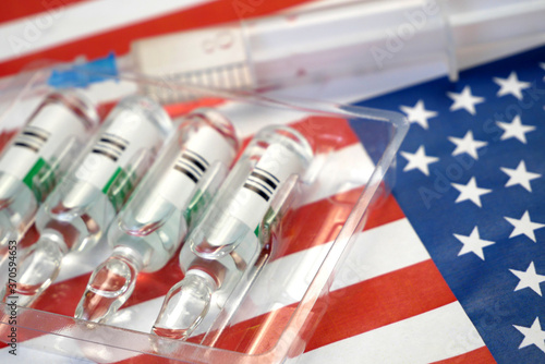 syringe with a vaccine is held by  hand in a glove on background of the USA flag, vaccine against coronavirus, Operation Warp Speed photo