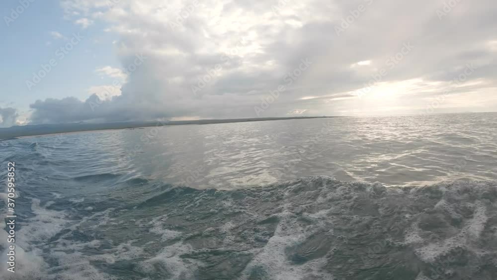 The sun is being covered by white clouds on an island of the Galapagos islands. Waves are formed due to the movement of a boat. The sun is being covered by white clouds on an island of the Galapagos islands. Waves are formed due to the movement of a boat.