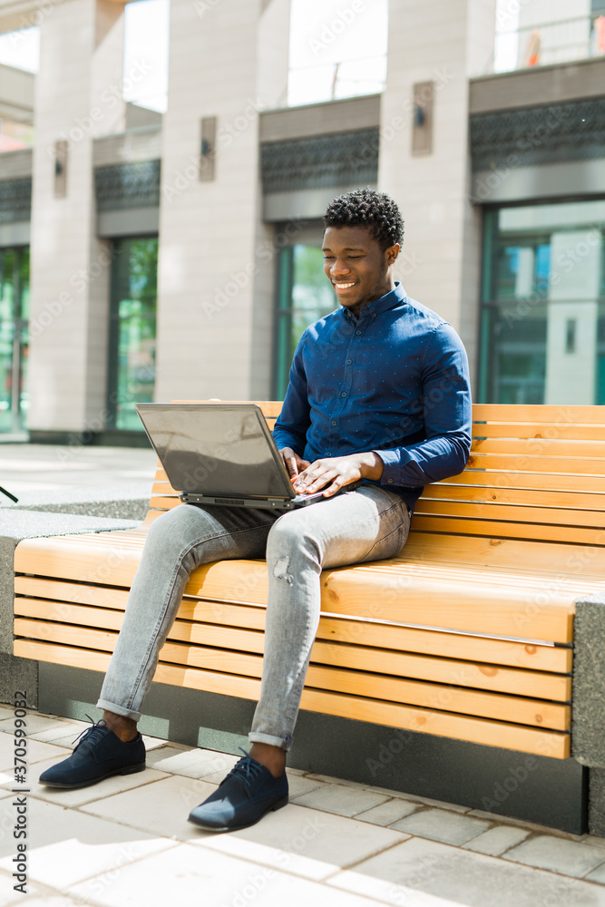 handsome young african man on bench with laptop