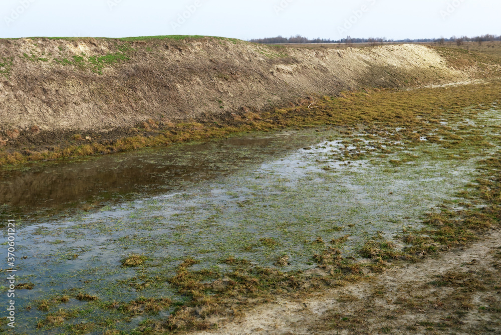 The exposed bottom of a dry pond. A shallow water body. A steep slope of the bank of an artificial pond. The exposed bottom of a dry pond. A shallow water body. A steep slope of the bank of an artificial pond.