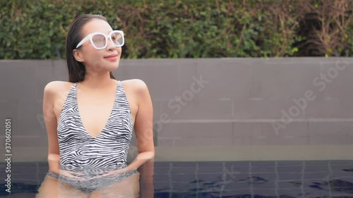 Medium close of a young woman in a zebra pattern one-piece swimsuit, lounging in the shallow end of a resort swimming pool. Copy space photo