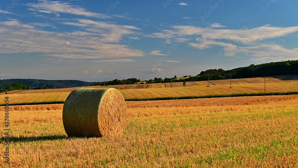 Hay bail harvesting in golden field landscape. Summer Farm Scenery with Haystack on the background of Beautiful Sunset.