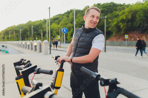 Electric urban transportation: the row of electric readies to ride scooter bikes with accumulators in the center of a city on the pavement stone with red electric bicycles behind