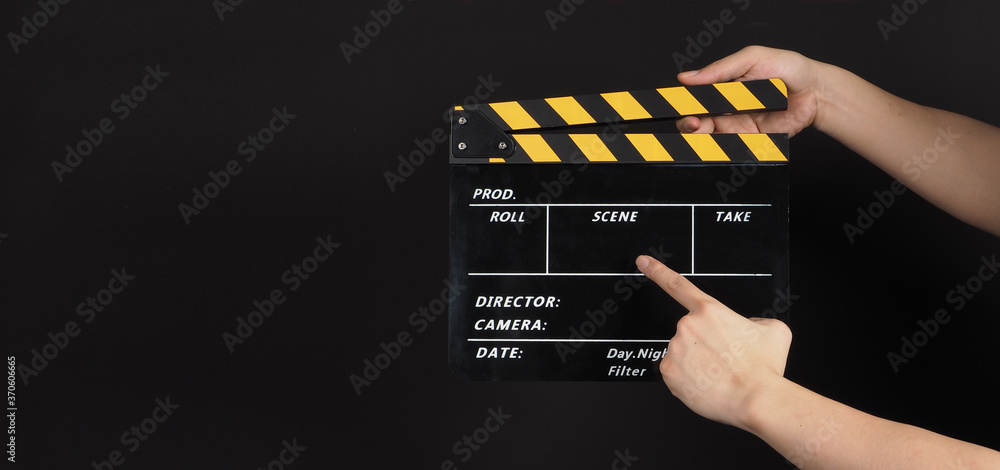Hand's holding and point at yellow&black Clapper board or movie slate use in video production and cinema industry on black background.
