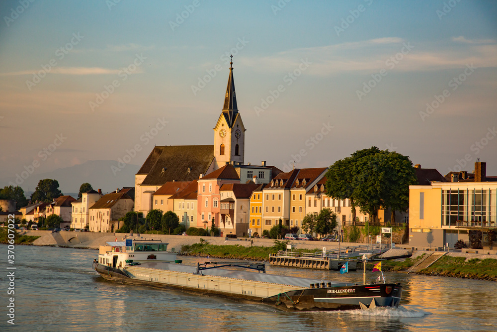 Sausenstein, Austria - 7/8/2013:  A river boat carrying freight on the Danube river and a church with clock tower, near Sausenstein, Austria,
