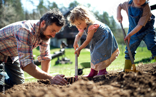 Father with small children working outdoors in garden, sustainable lifestyle concept.