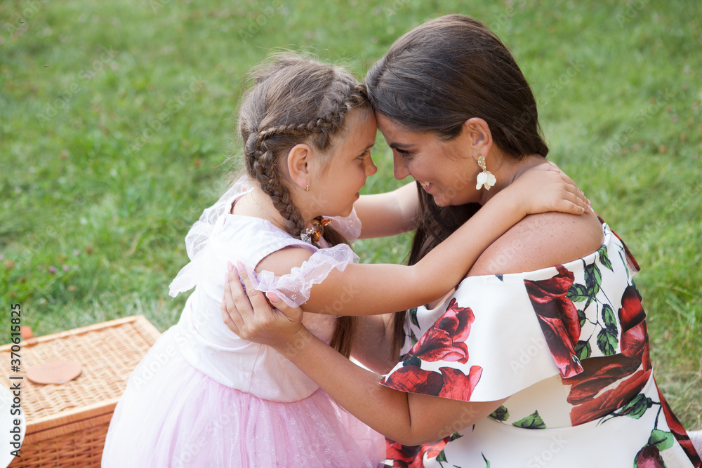 Fototapeta premium Mother and daughter hugging and cuddling head to head outdoors at the picnic