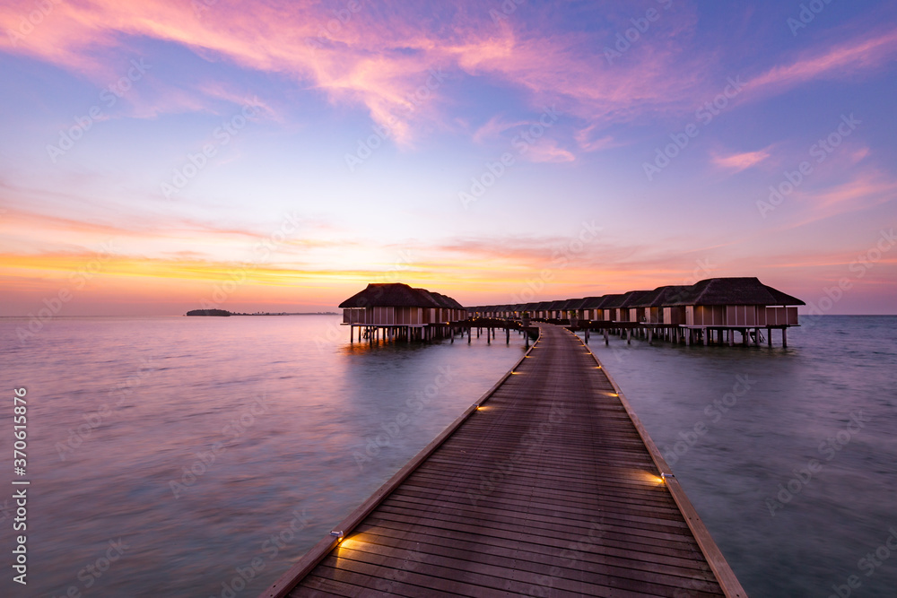 Sunset on Maldives island, luxury water villas resort and wooden pier. Beautiful sunset sky and clouds and tropical beach background for summer vacation holiday and travel concept banner
