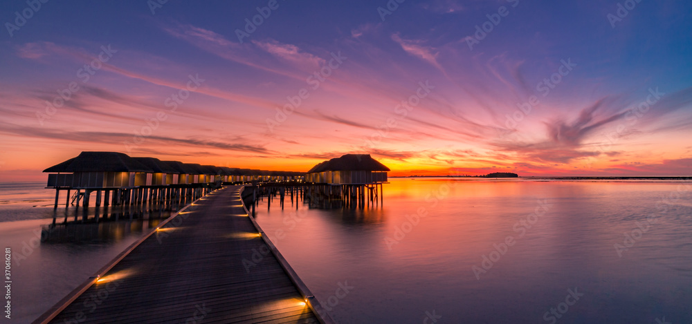 Sunset on Maldives island, luxury water villas resort and wooden pier. Beautiful sunset sky and clouds and tropical beach background for summer vacation holiday and travel concept banner
