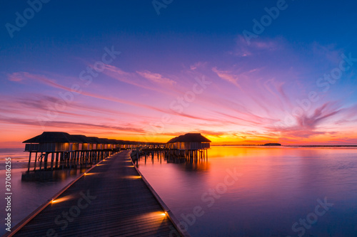 Sunset on Maldives island  luxury water villas resort and wooden pier. Beautiful sunset sky and clouds and tropical beach background for summer vacation holiday and travel concept banner 