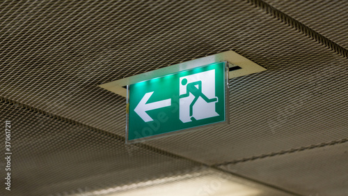 Illuminated emergency exit sign. Green sign with white arrow and figure running to the left. Symbol for escape, danger, running away