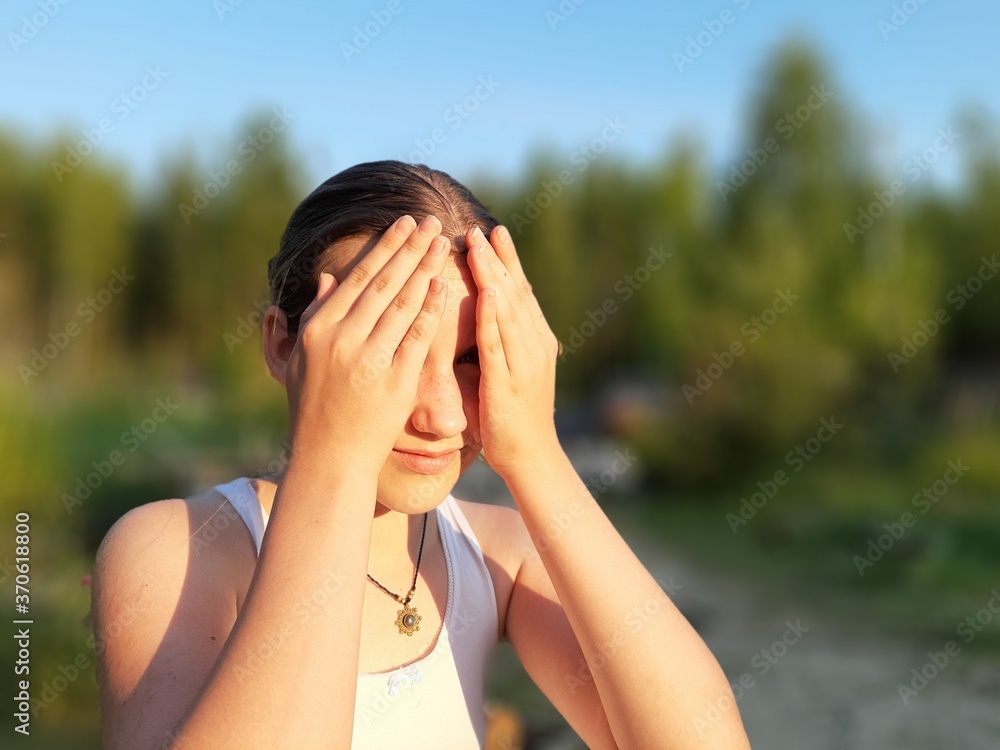 The girl is playing hide-and-seek. Covers his face with his hands. Summer, park, day.