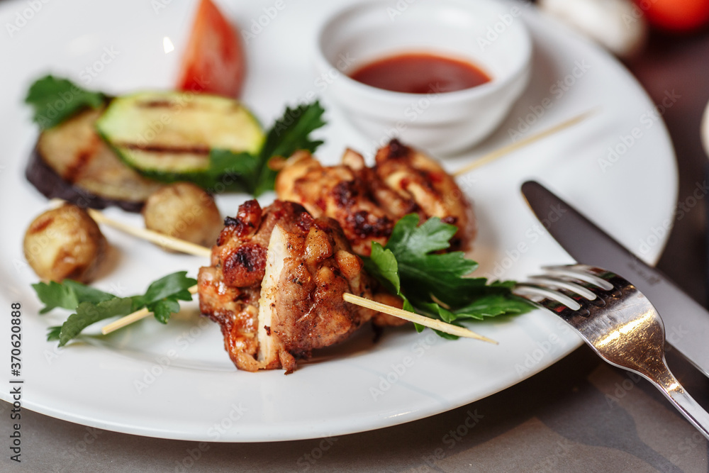 Barbecued marinated turkey or chicken meat shish kebab skewers with ketchup sauce and grilled vegetables on rustic wooden table background. Traditional barbecue grill food