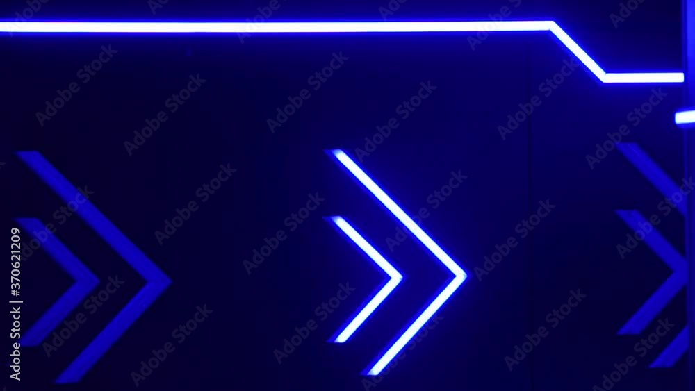 Illuminated direction indicator. Neon arrows blink to the right on a dark blue background in night club. Illuminated direction indicator. Neon arrows blink to the right on a dark blue background in night club.