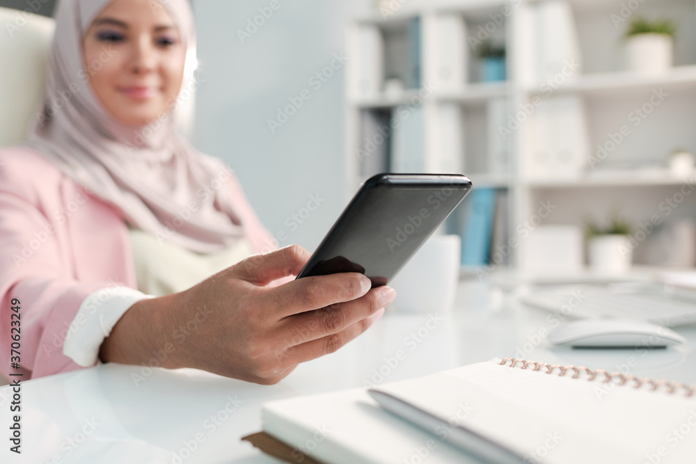 Close-up of Muslim woman using smslartphone while answering sms in office Close-up of Muslim woman using smslartphone while answering sms in office