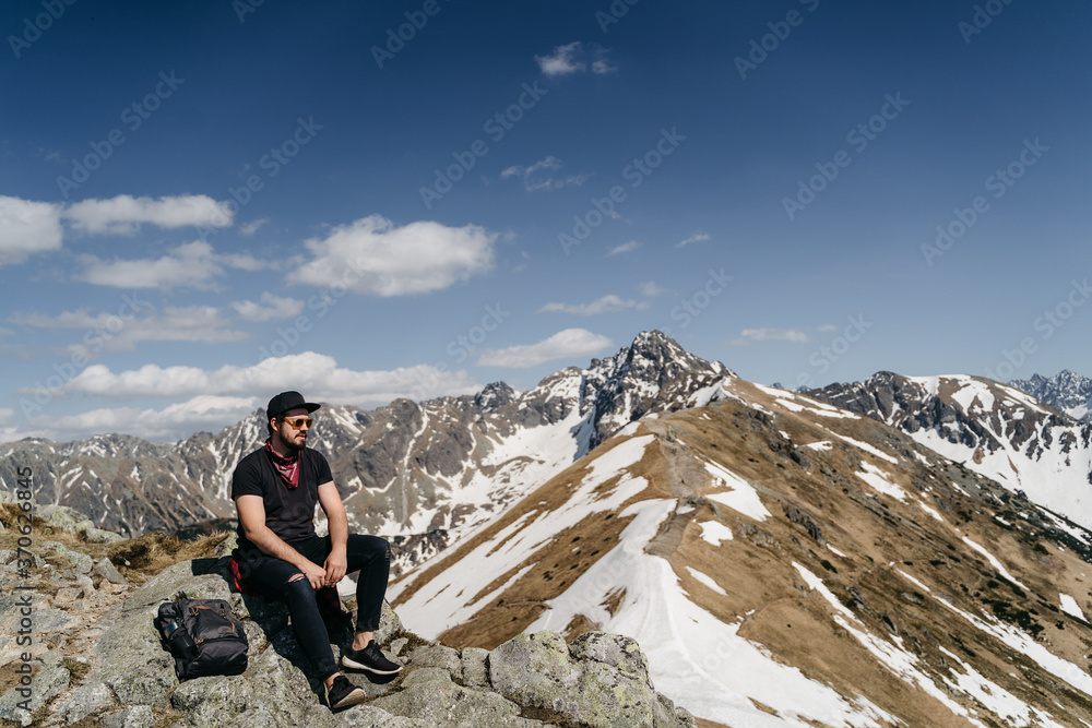 Fototapeta premium young hister guy with a beard in the mountains with a backpack. Active rest in one with nature