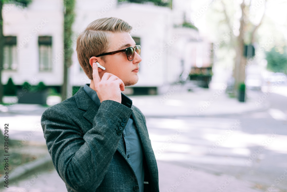 Fototapeta premium Close up portrait of young man in suit using earphones in city.